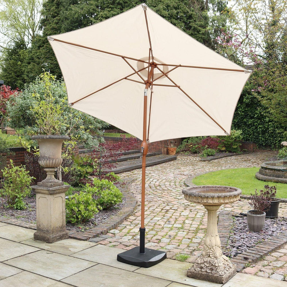 Cream garden parasol with wooden pole on stone patio beside birdbath and plants