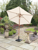 Cream garden parasol with wooden pole on stone patio beside birdbath and plants