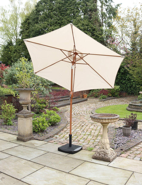 Cream garden parasol with wooden pole on stone patio beside birdbath and plants