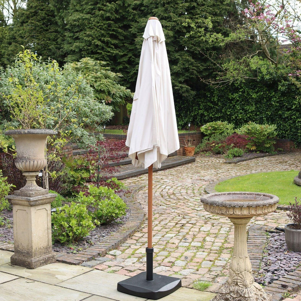 Cream garden parasol with wooden pole and base on stone patio beside birdbath