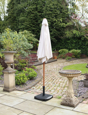 Cream garden parasol with wooden pole and base on stone patio beside birdbath