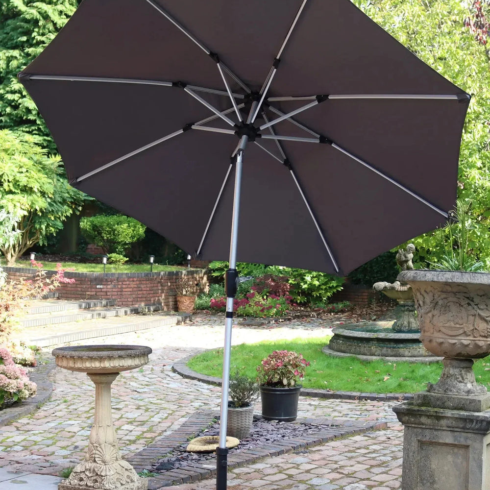Grey garden parasol with metal frame and crank base on patio beside stone bird bath