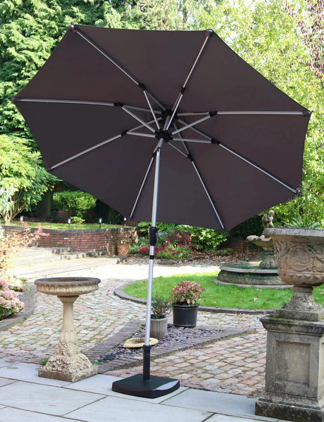 Grey garden parasol with metal frame and crank base on patio beside stone bird bath