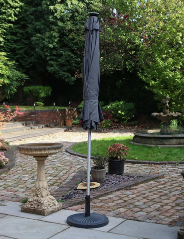 Grey garden parasol with metal pole and base on stone patio in landscaped backyard