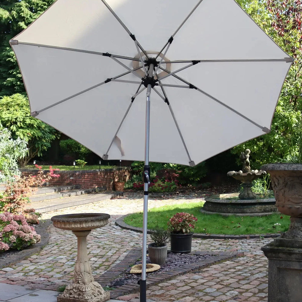 Beige outdoor garden parasol with metal frame on patio, surrounded by plants and stone decor