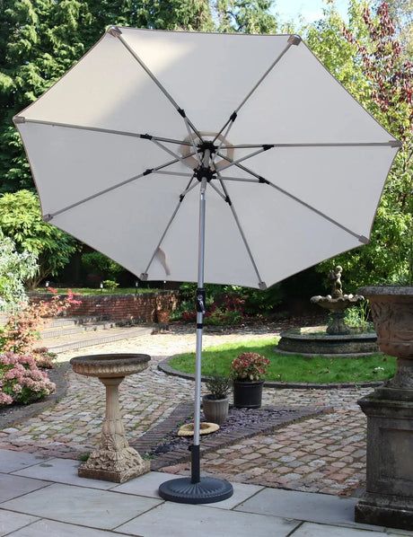 Beige outdoor garden parasol with metal frame on patio, surrounded by plants and stone decor