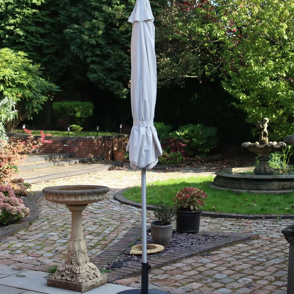 Closed outdoor garden parasol with white canopy and black base on stone patio