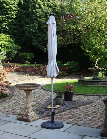 Closed outdoor garden parasol with white canopy and black base on stone patio