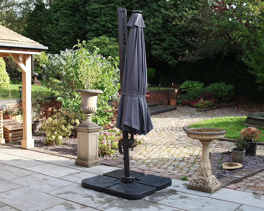 Grey cantilever garden parasol closed on patio with paving and surrounding planters