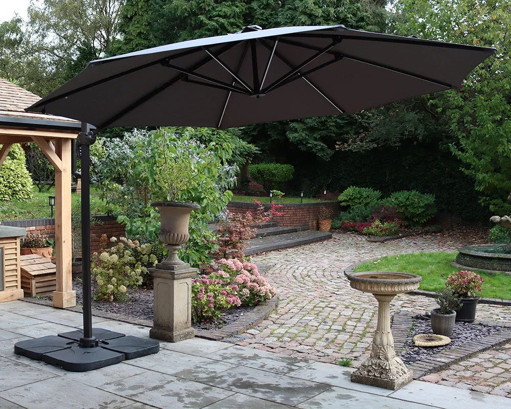 Large black cantilever garden parasol on patio with paved path and landscaped plants