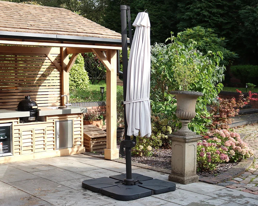 Closed cantilever garden parasol with black base on patio next to outdoor kitchen and plants