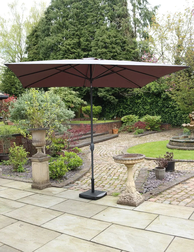 Brown garden parasol with black pole on patio in landscaped outdoor setting