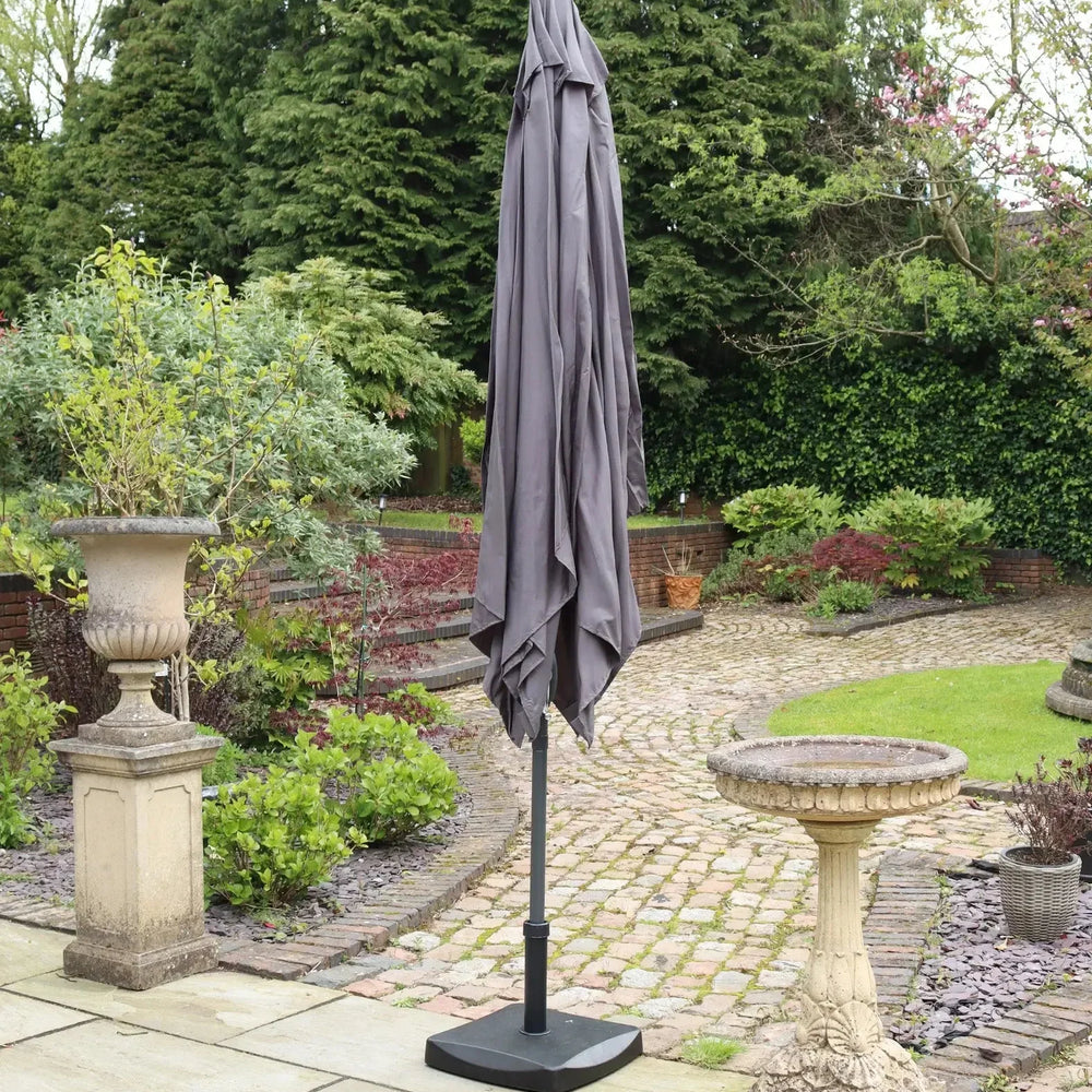 Closed grey garden parasol with weighted base on stone patio in landscaped backyard