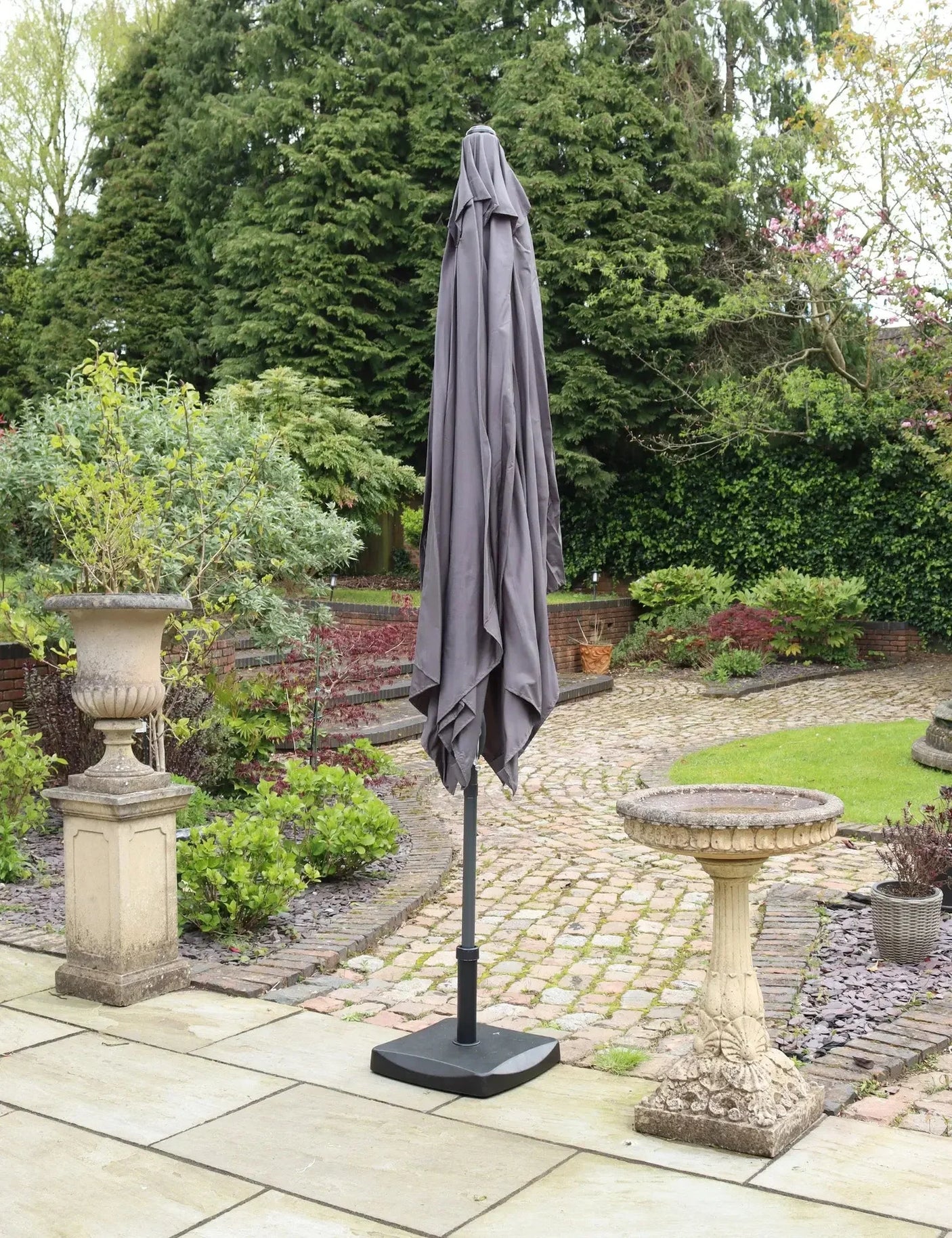 Closed grey garden parasol with weighted base on stone patio in landscaped backyard