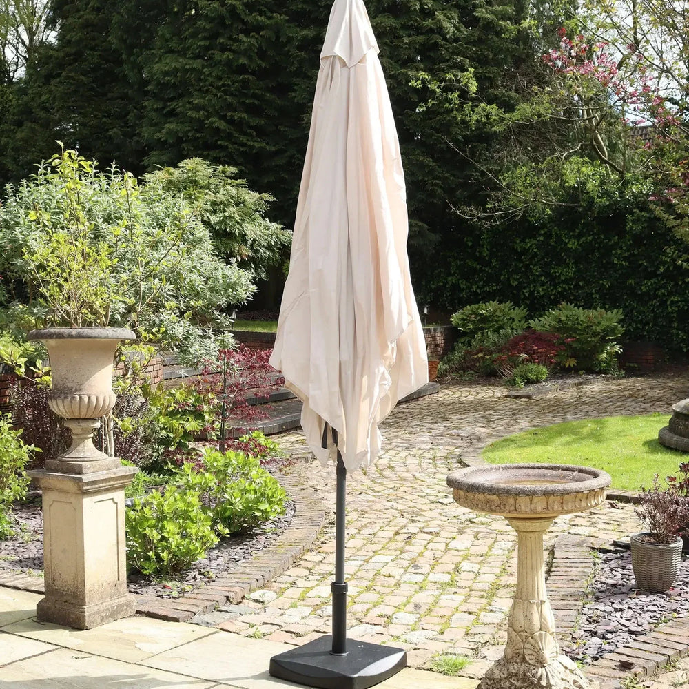 Beige garden parasol closed on a patio with stone birdbath and planter