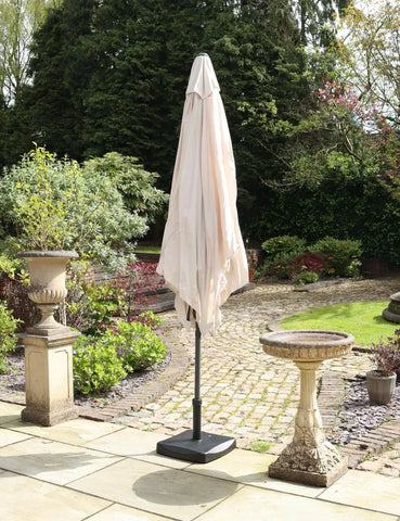 Beige garden parasol closed on a patio with stone birdbath and planter