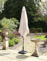 Beige garden parasol closed on a patio with stone birdbath and planter