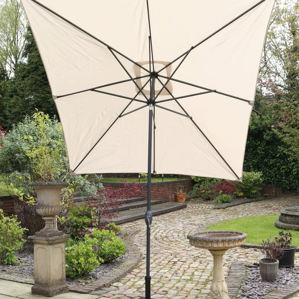 Beige garden parasol with black pole and square base on stone patio