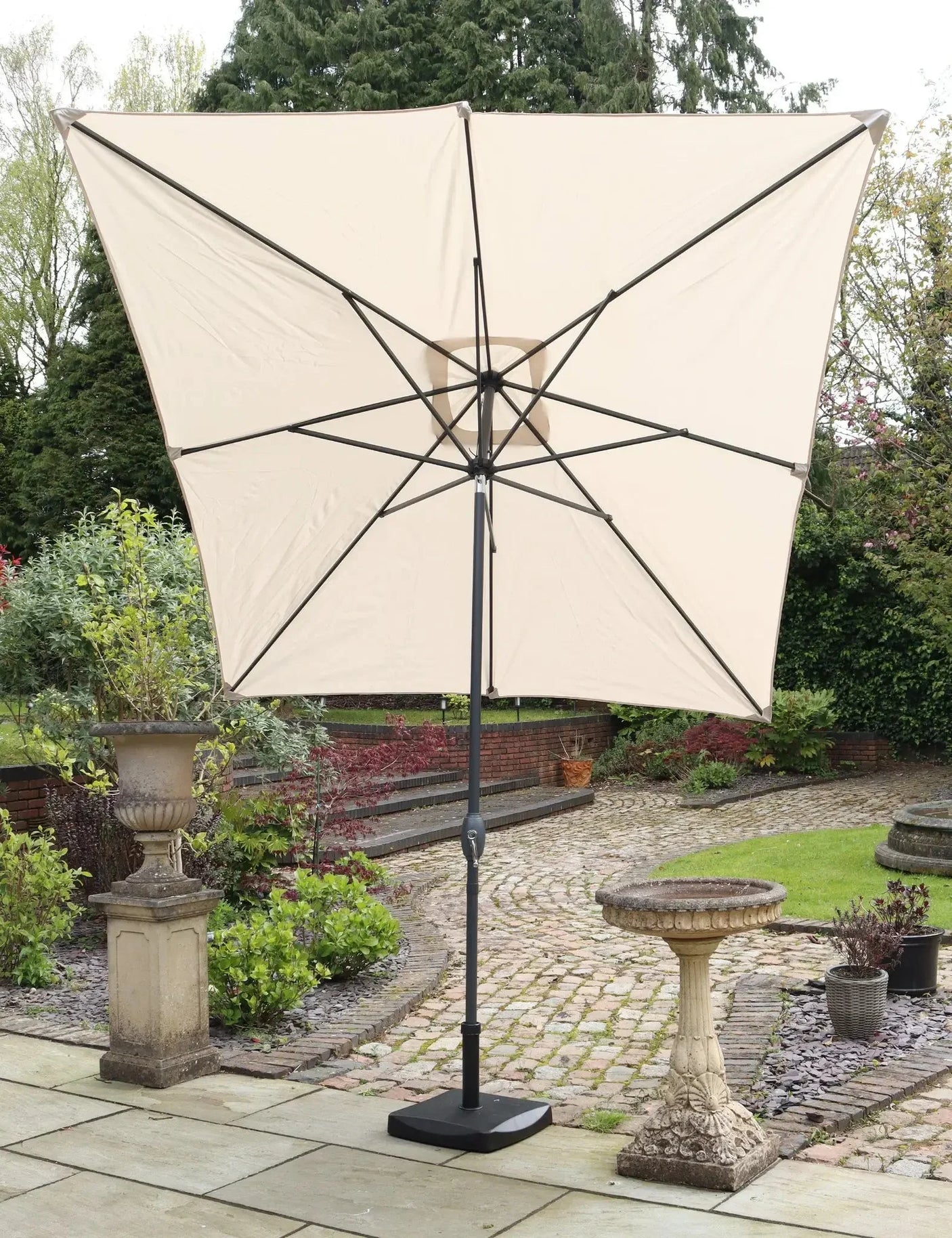 Beige garden parasol with black pole and square base on stone patio
