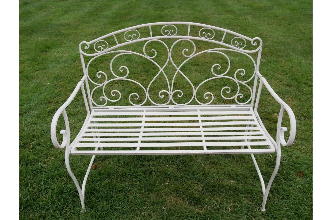 White metal garden bench with scrollwork back and arms on green lawn