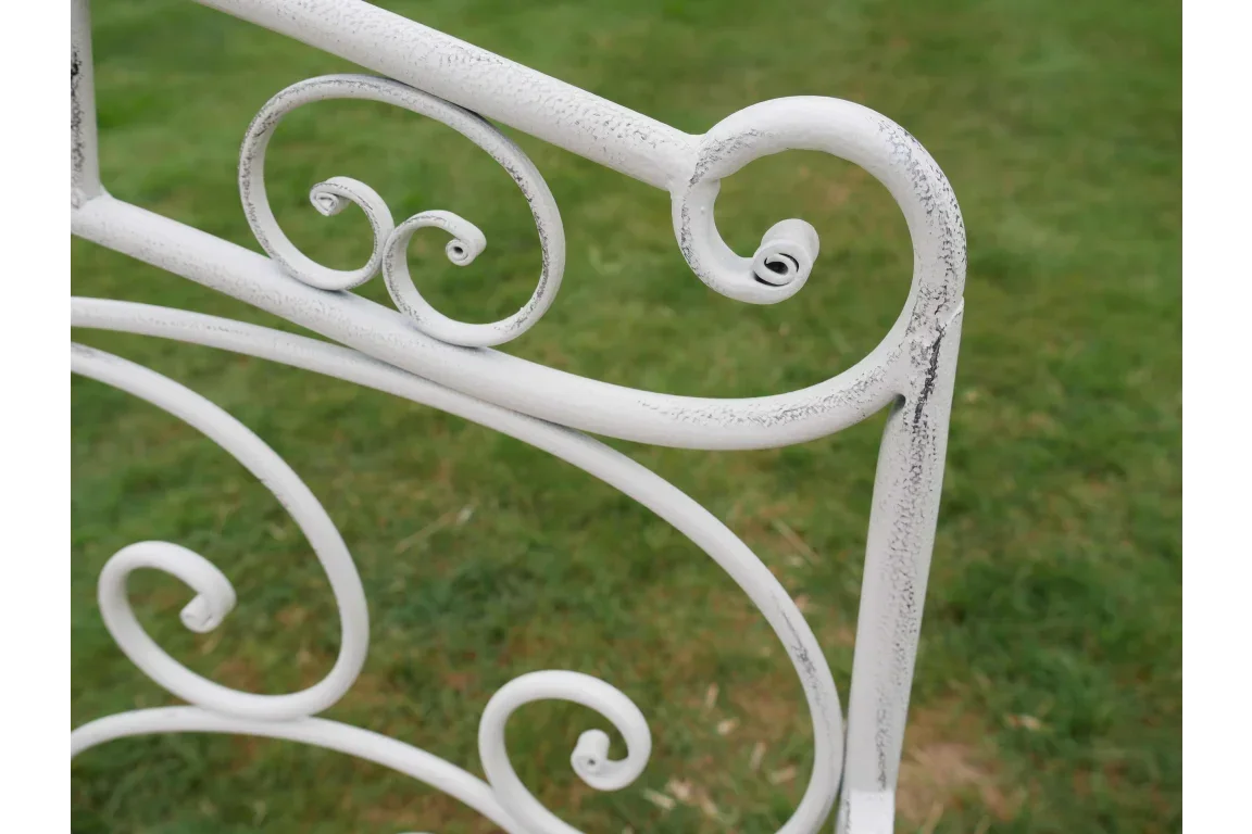 White metal garden bench with decorative scrollwork detail on grassy lawn