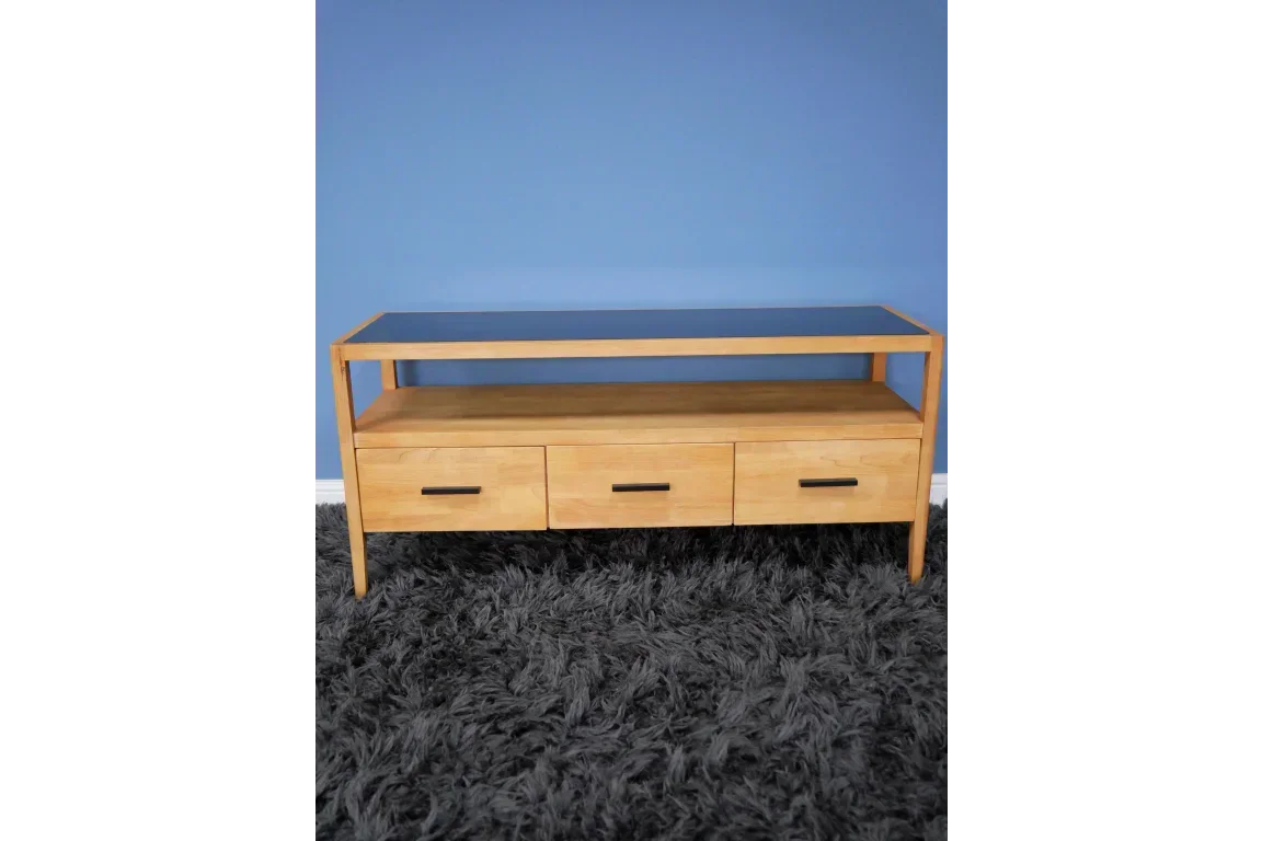 Oak TV unit with glass top and three drawers on grey carpet, blue wall background