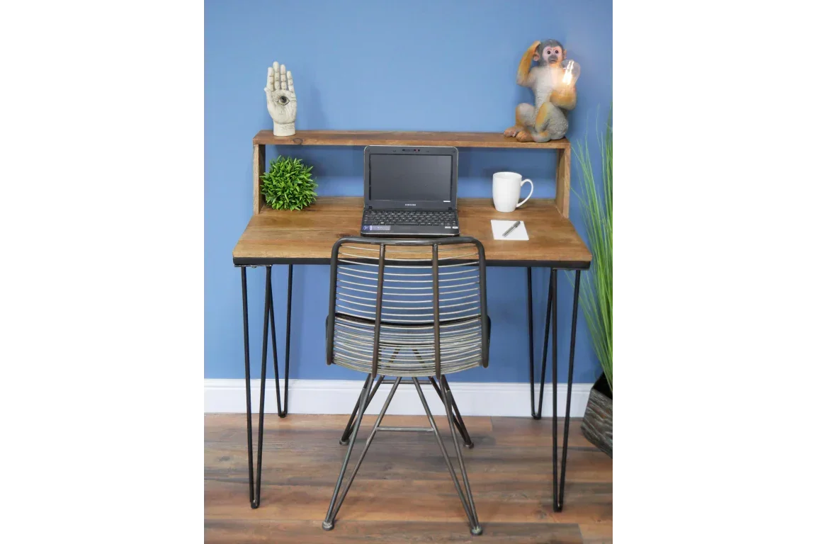 Industrial wooden desk with metal legs, laptop, mug, and decor against blue wall