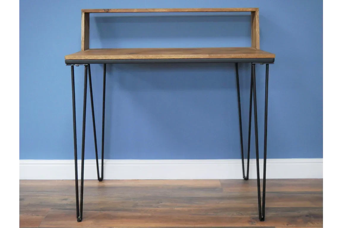 Wooden desk with black metal hairpin legs and raised shelf against blue wall