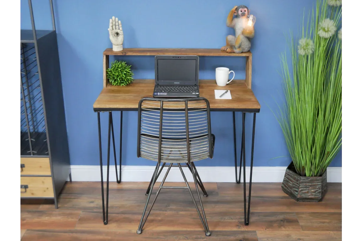 Industrial desk with metal legs, laptop, wire chair, and home office decor against blue wall