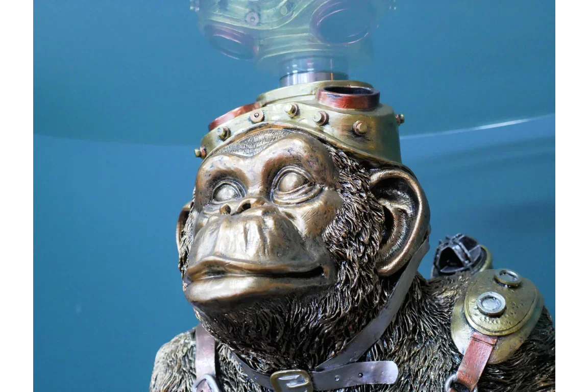 bronze steampunk monkey ornament with goggles and metal details against blue background