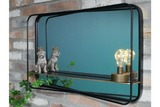 Rectangular black metal framed wall mirror with shelf holding two dog figurines and a decorative light bulb.