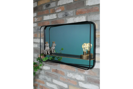 Rectangular wall mirror with black metal frame and built-in shelf, mounted on exposed brick wall, side angle view.