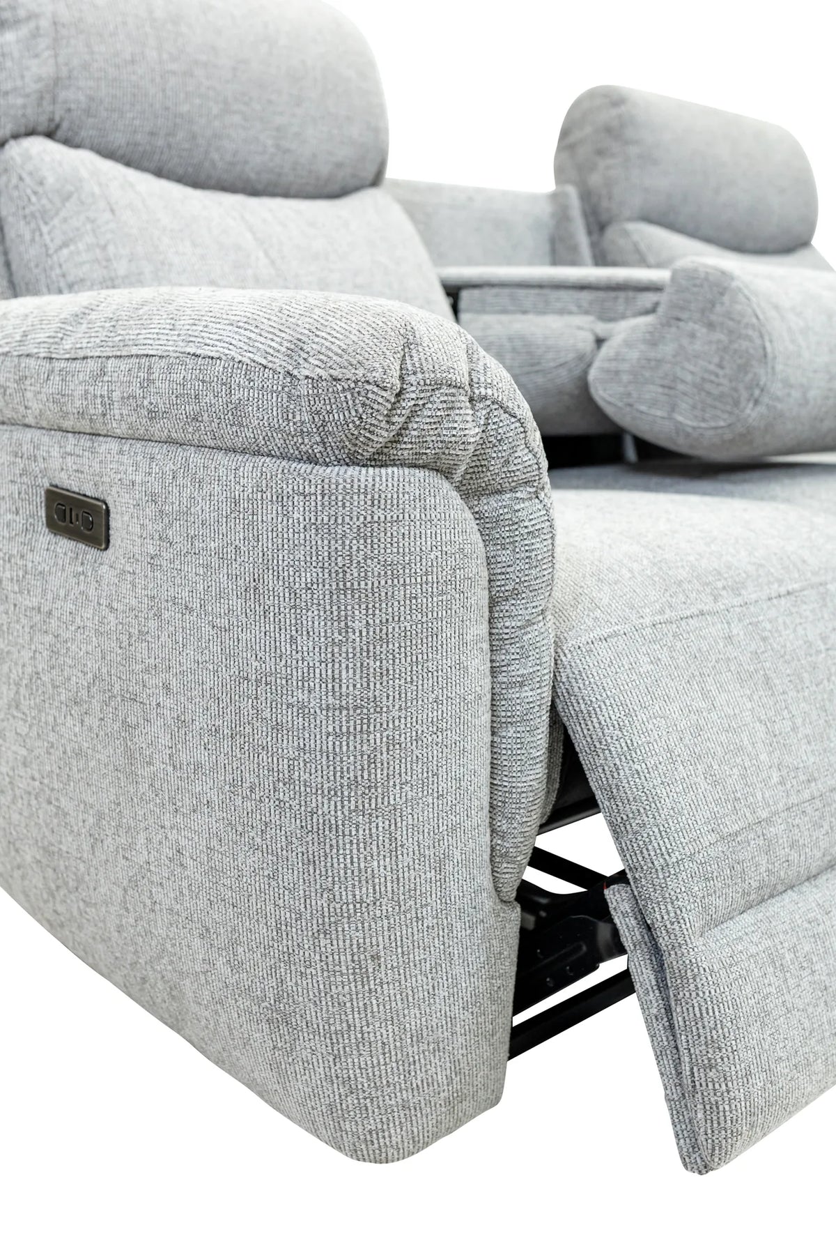 Close-up of a light gray textured recliner chair showing the side armrest, power control plaque, and extended footrest against a white background.