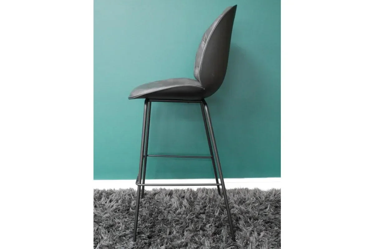 Grey bar stool with cushioned seat and metal legs, side view on textured rug