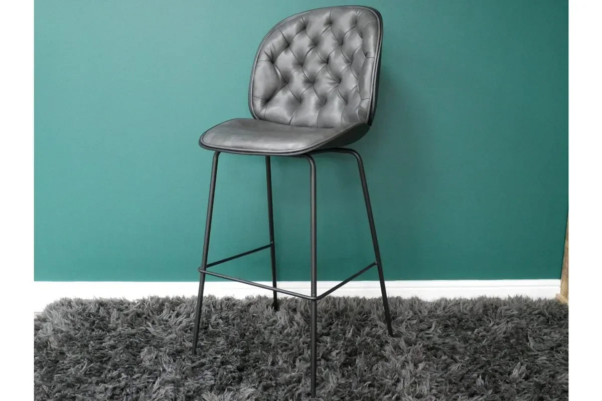 Grey leather bar stool with tufted backrest and black metal legs on shaggy rug