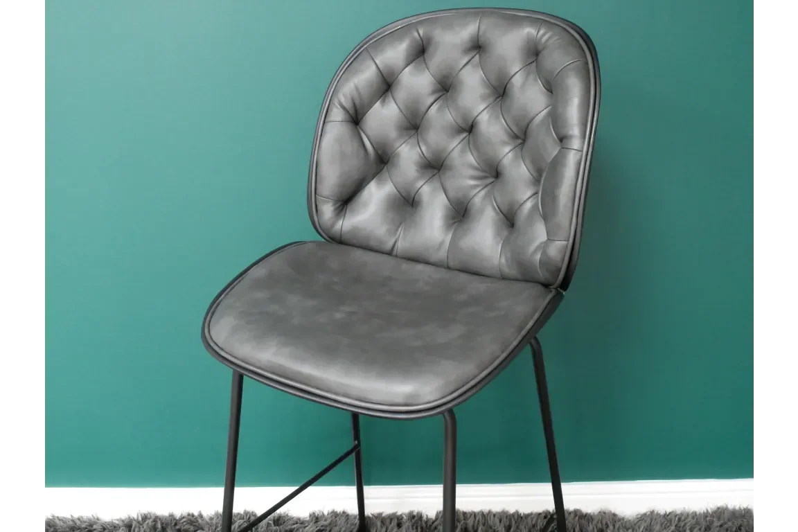 Grey leather dining chair with black metal legs and tufted backrest against green wall