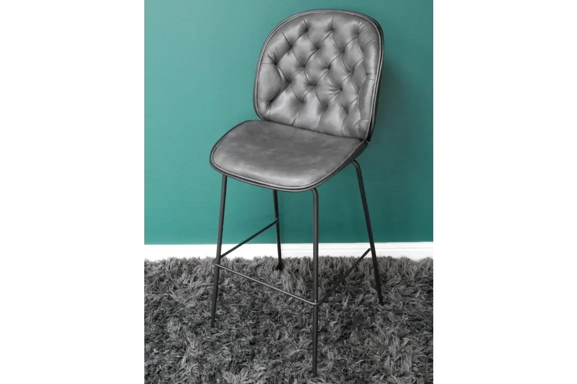 Grey faux leather bar stool with tufted back and black metal legs on a shaggy rug