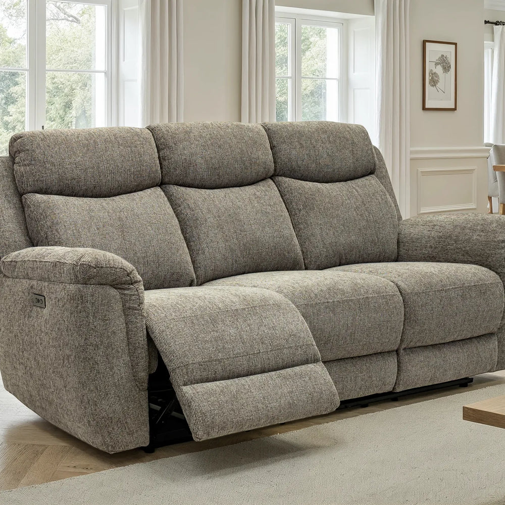 A three-seat reclining loveseat in textured light gray upholstery, shown with the front footrest extended in a bright, modern living room.