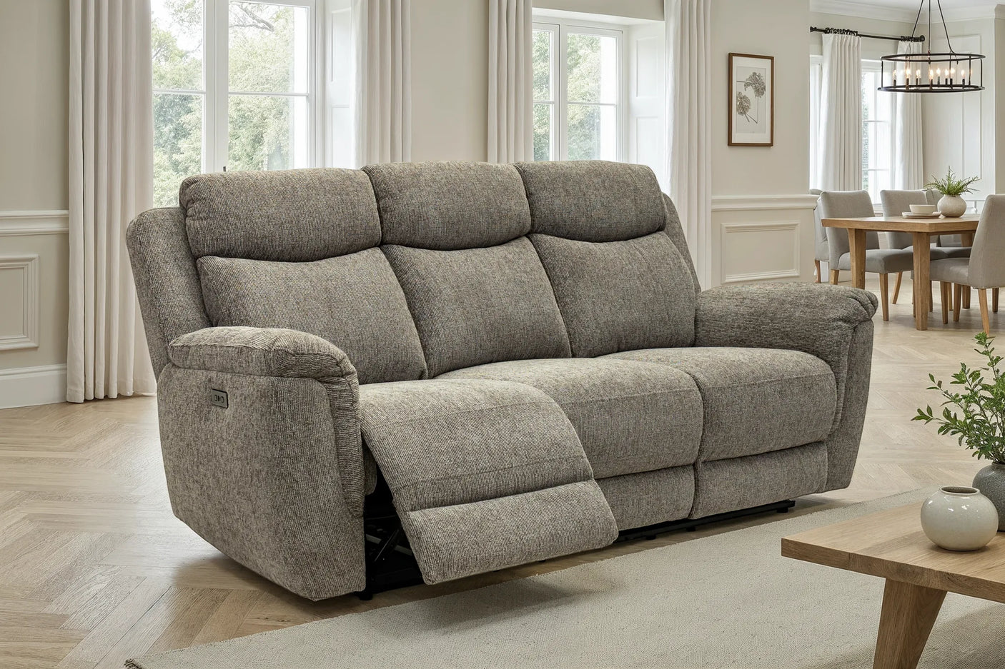 A three-seat reclining loveseat in textured light gray upholstery, shown with the front footrest extended in a bright, modern living room.