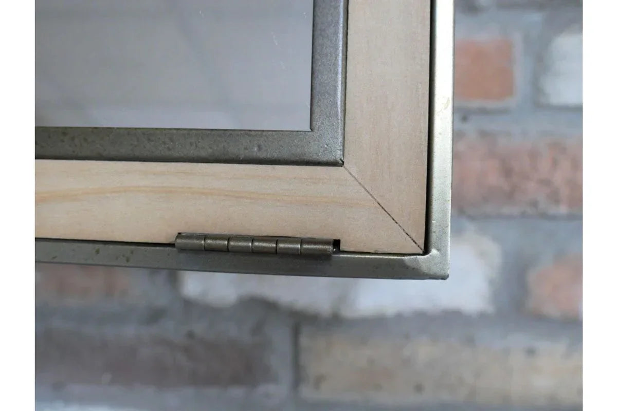 Closeup of glass cabinet door corner with wood frame and metal hinge against brick wall