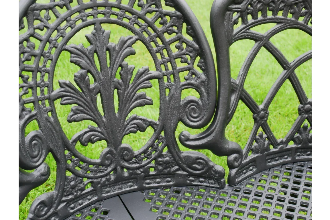 Cast iron garden bench closeup with intricate decorative backrest on grass