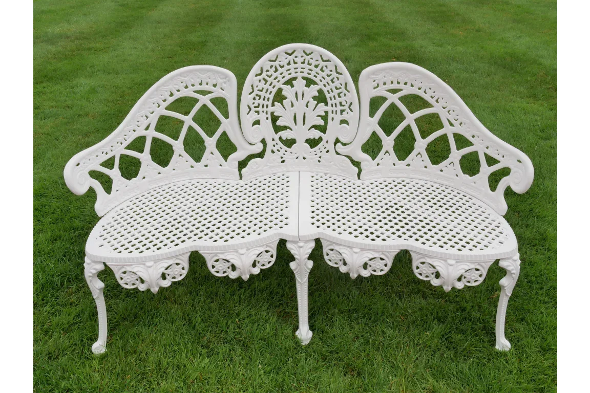 White cast iron garden bench with ornate floral design on grass lawn