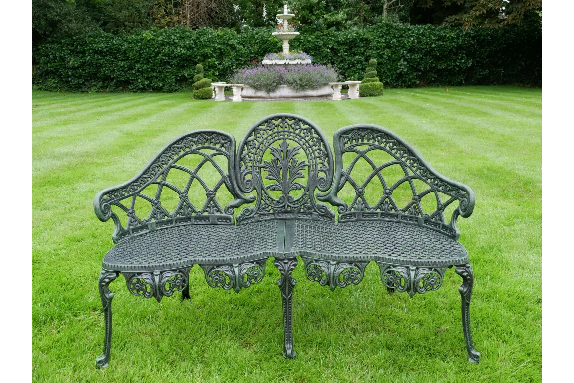 Cast iron garden bench with ornate detailing on lawn, garden fountain in background