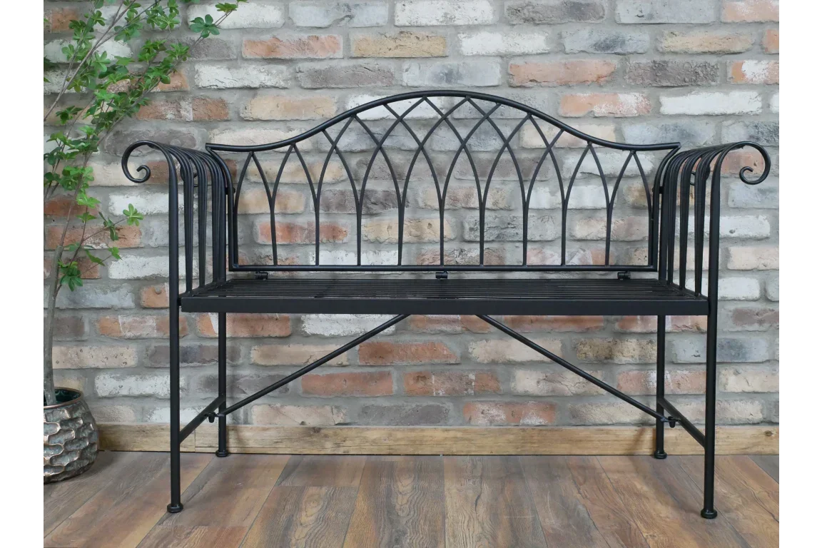 Black metal garden bench with decorative arched backrest against brick wall