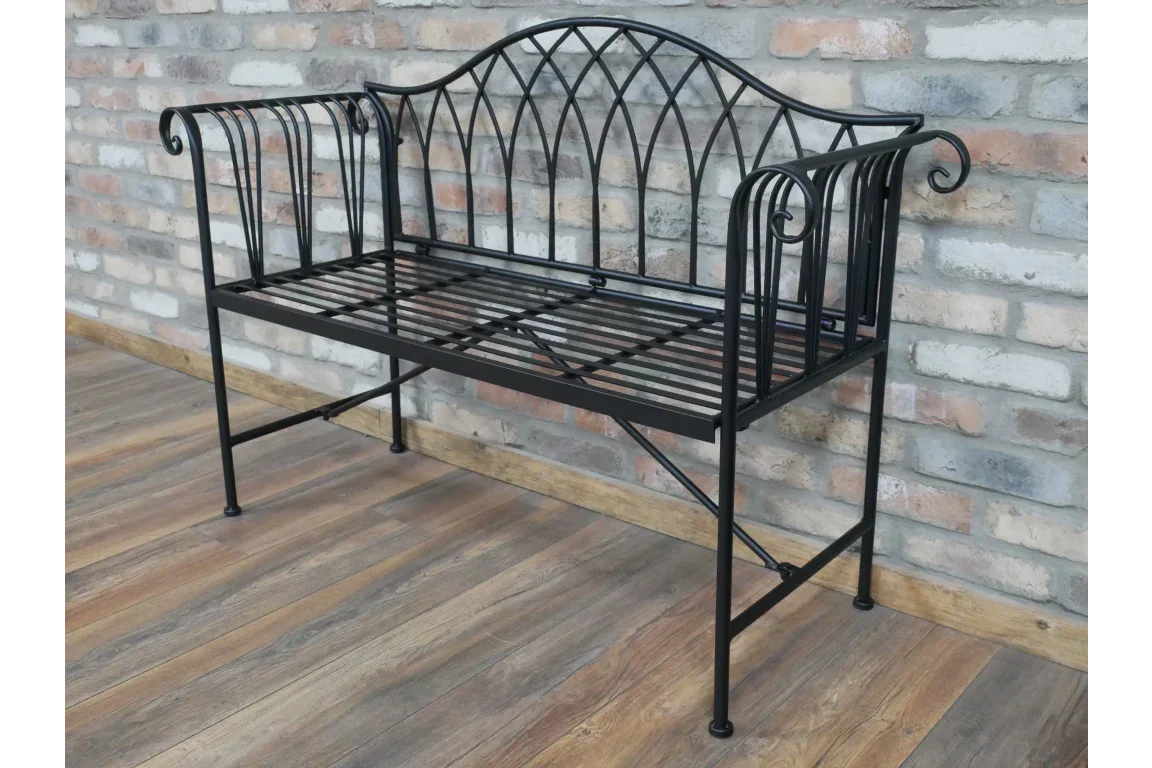 Black metal garden bench with decorative backrest and scroll armrests on wood flooring