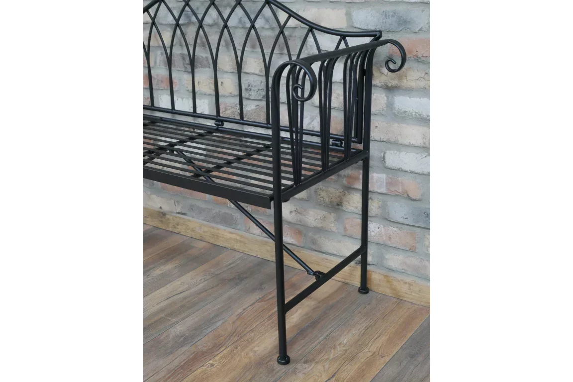 Black metal garden bench with decorative backrest and slatted seat against brick wall