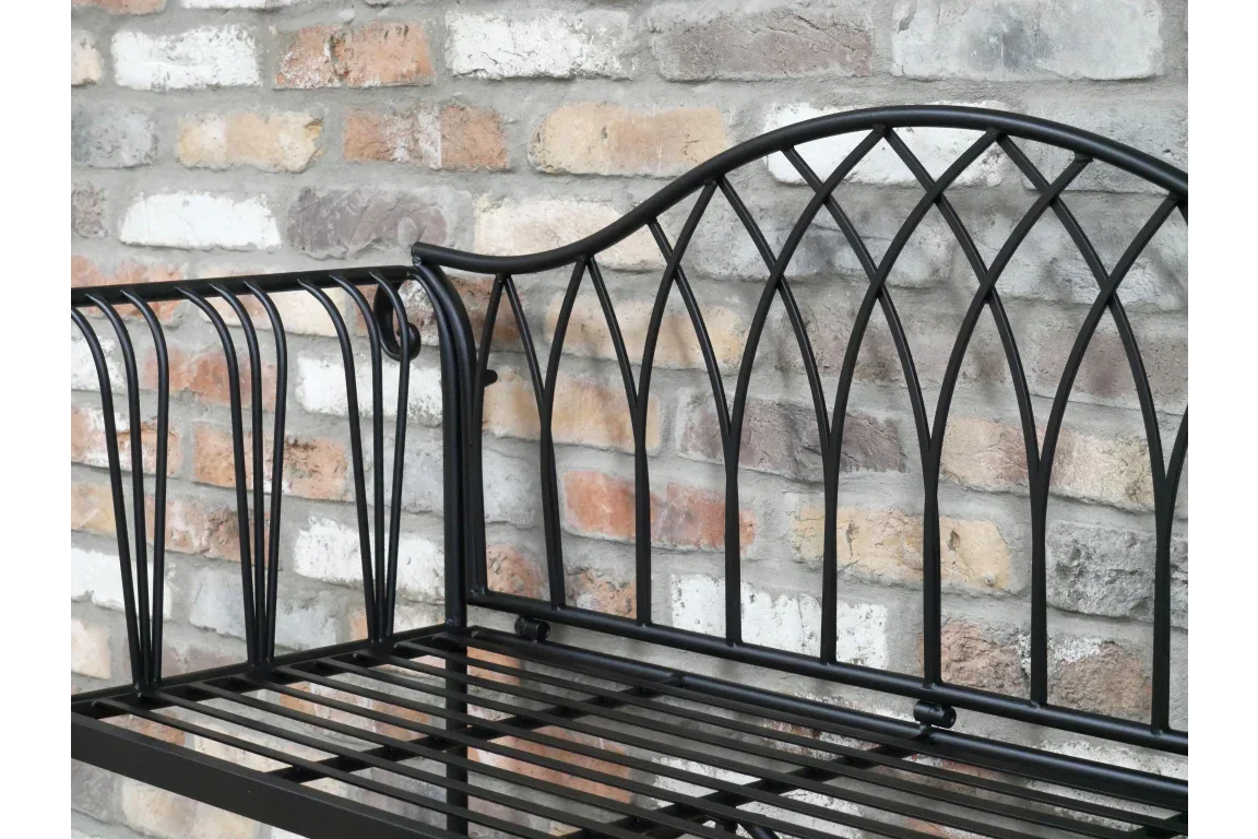 Black metal garden bench with decorative backrest against brick wall