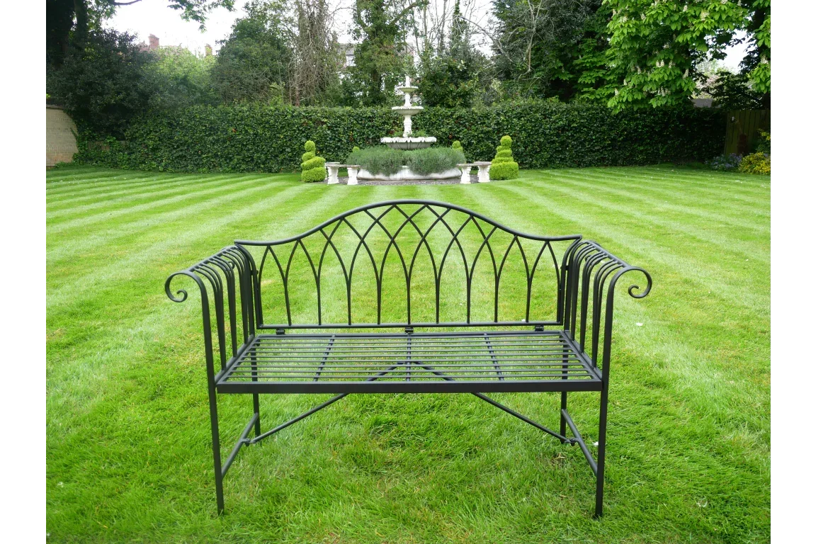 Black metal garden bench with decorative frame on lawn near fountain