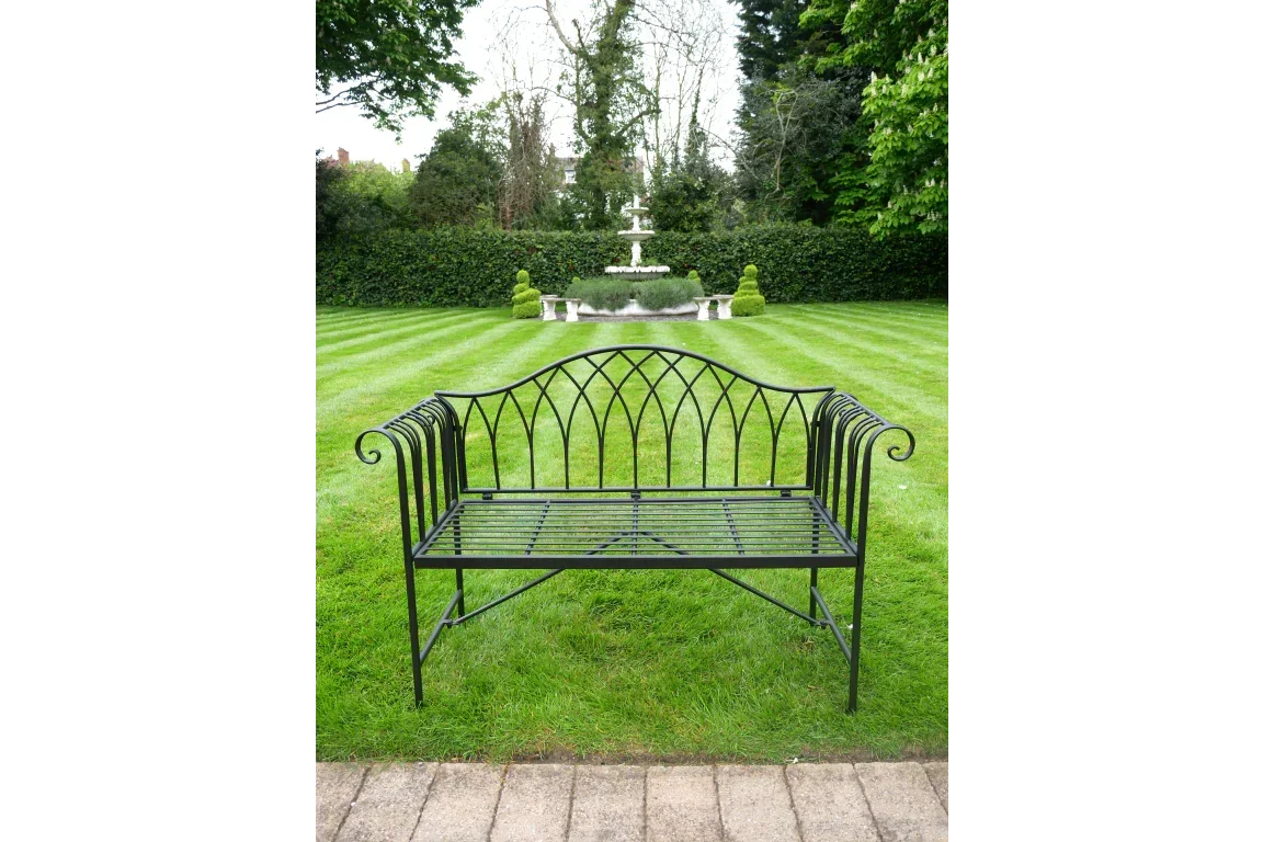 Black metal garden bench with decorative backrest on lawn, fountain in background