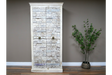 Large white wooden cabinet with intricate carved details and metal ring handles, standing on wooden floor beside green plant.